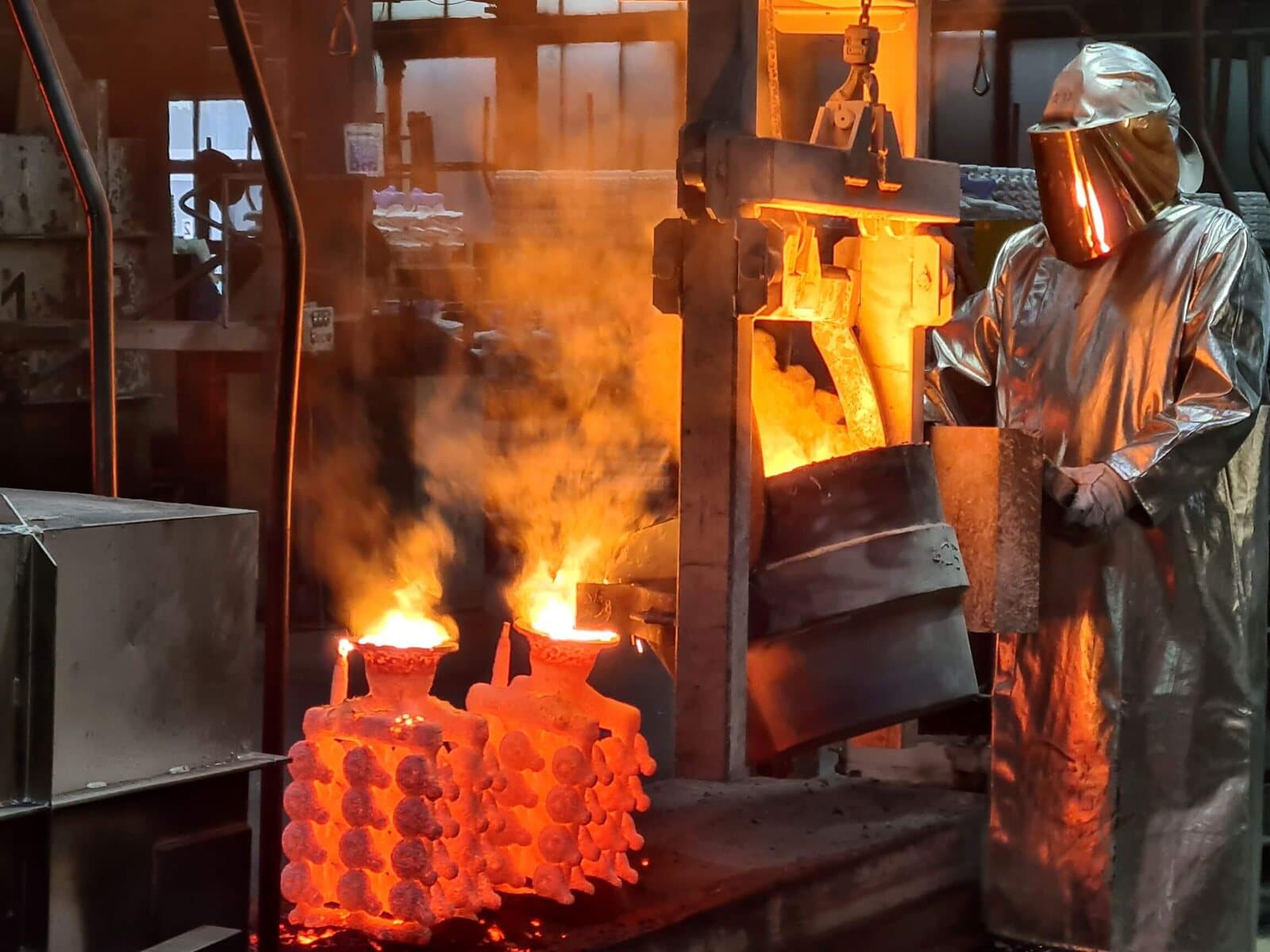 A foundry worker in a heat-reflective suit pouring molten steel into preheated ceramic shell molds